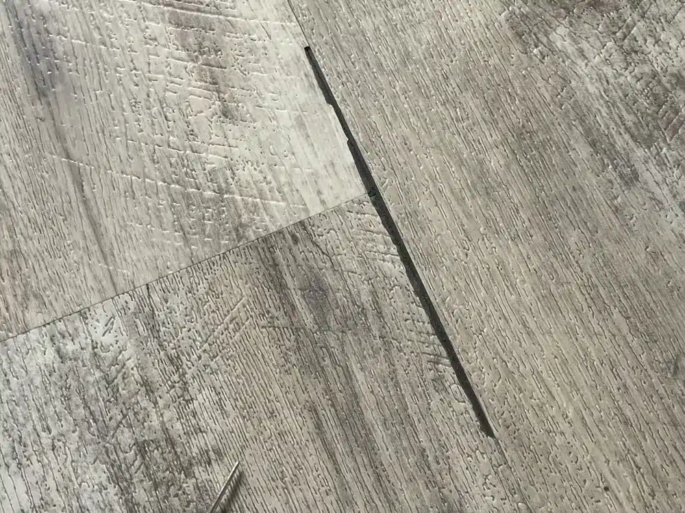 An actual rigid-core flooring inspection showing a broken plank edge